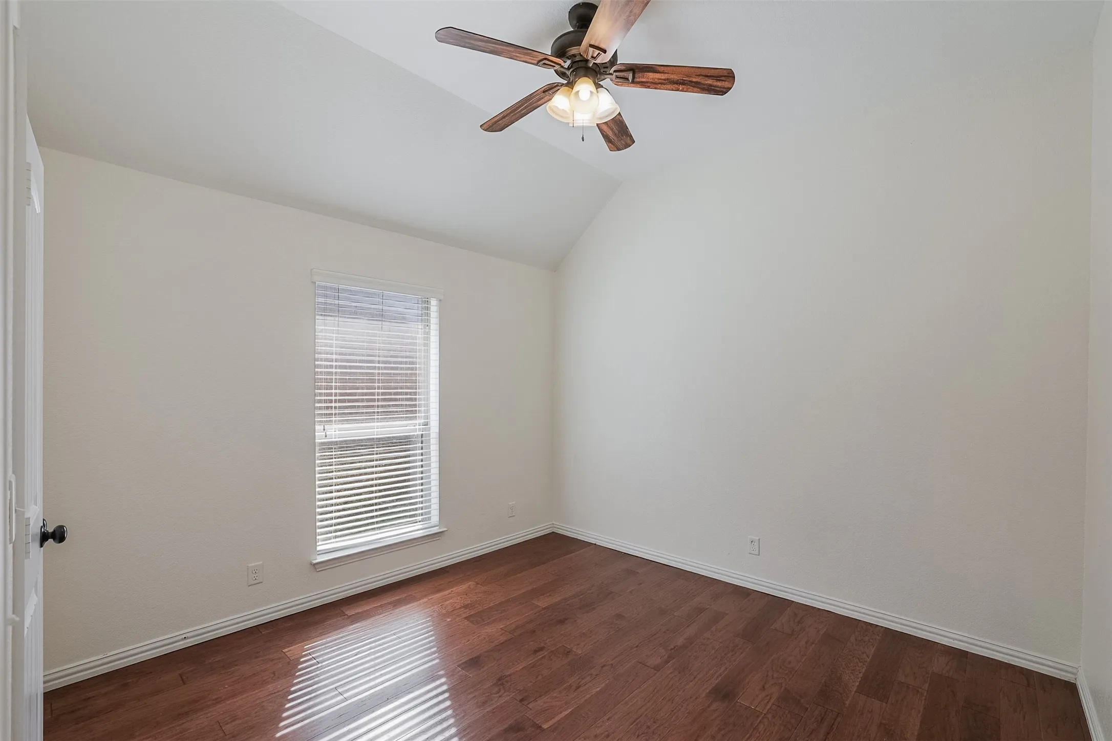 Vaulted ceiling, wood-finish flooring, ceiling fan with integrated lighting, window with blinds, panel door