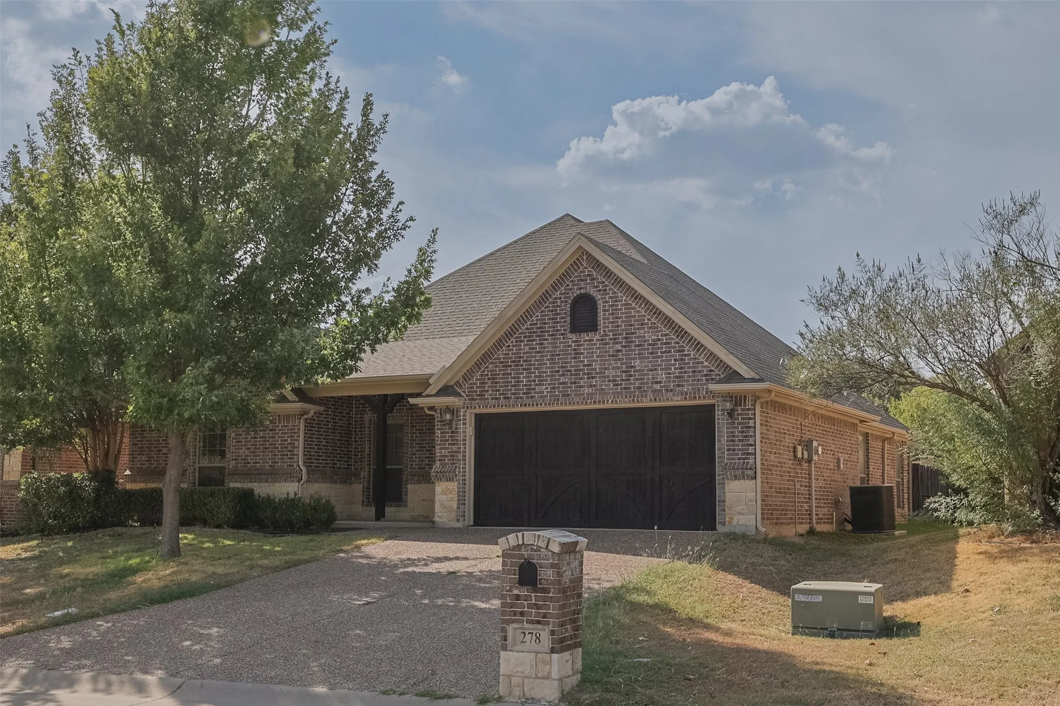 Brick and stone exterior featuring an arched entryway, covered porch, and a two-car garage