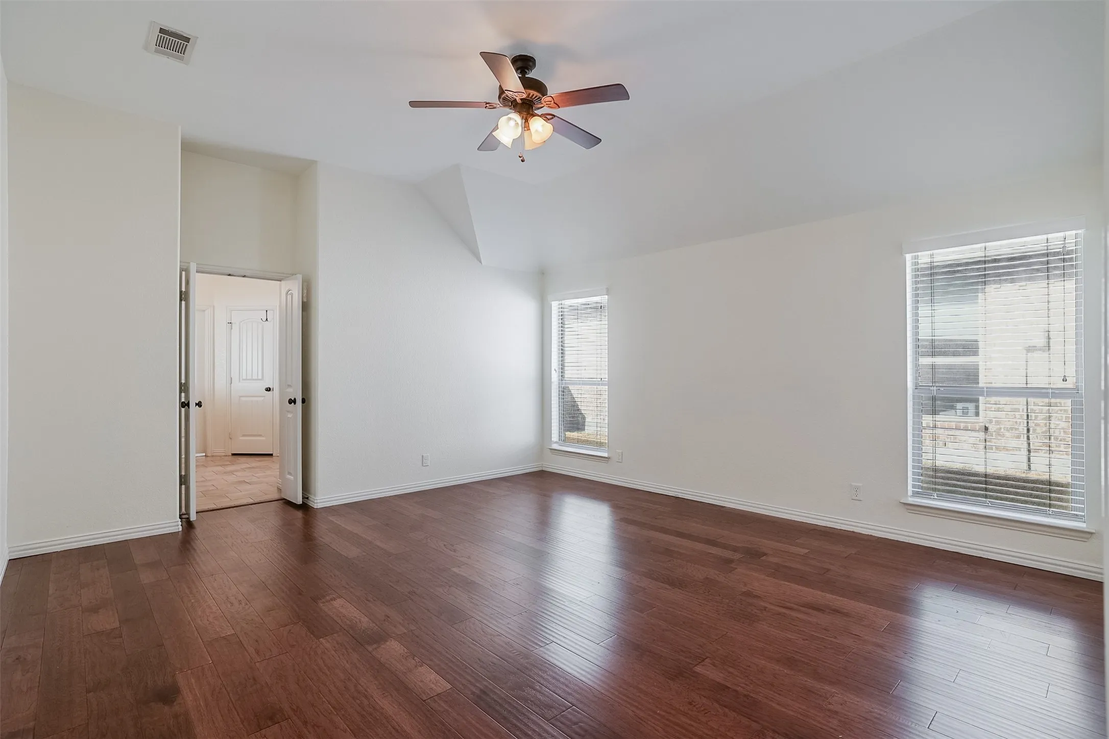 Spacious room featuring wood-finish flooring, white walls, and a ceiling fan