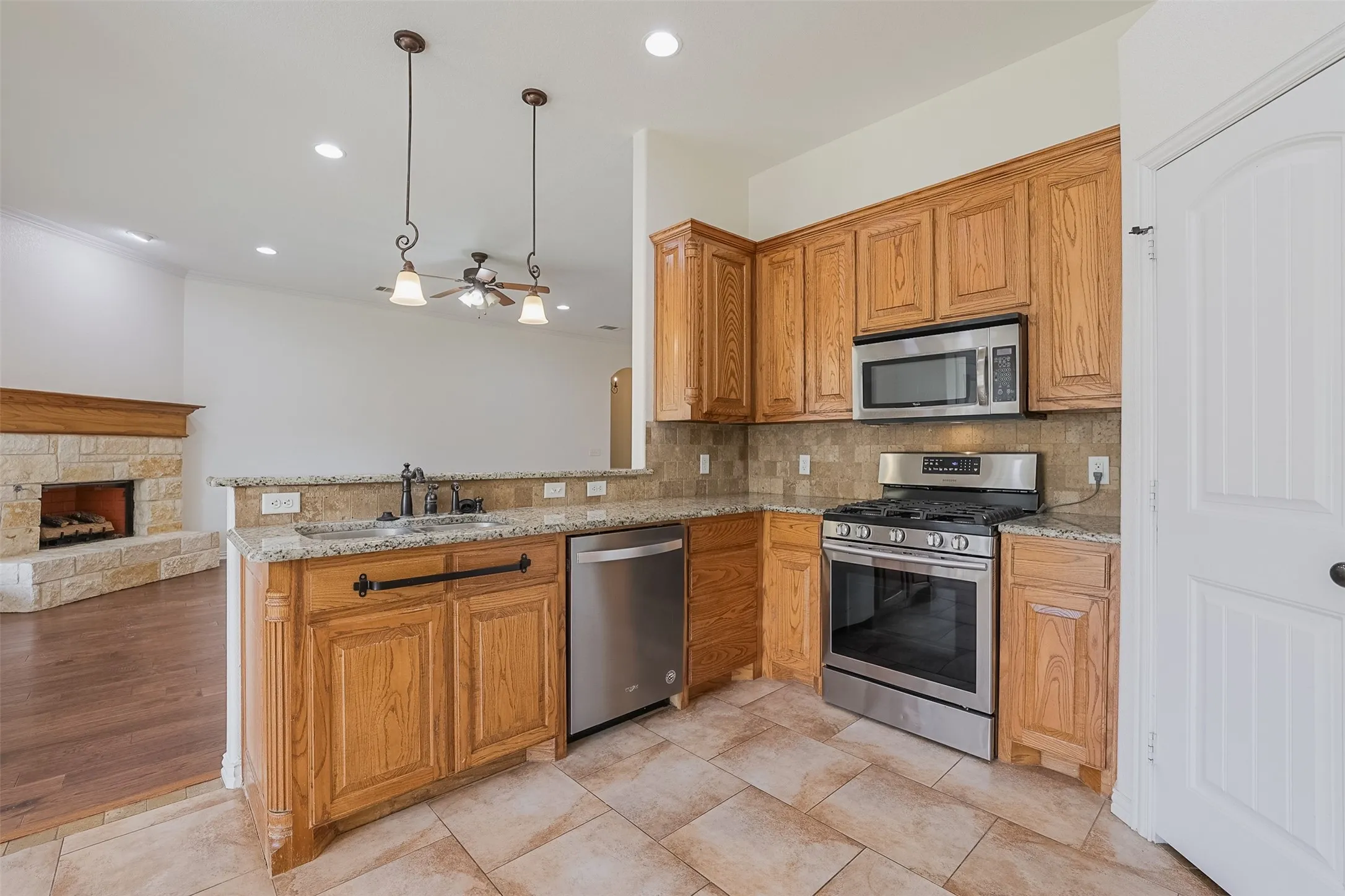 Kitchen featuring light wood cabinetry, stainless steel appliances, stone tile flooring, and granite countertops