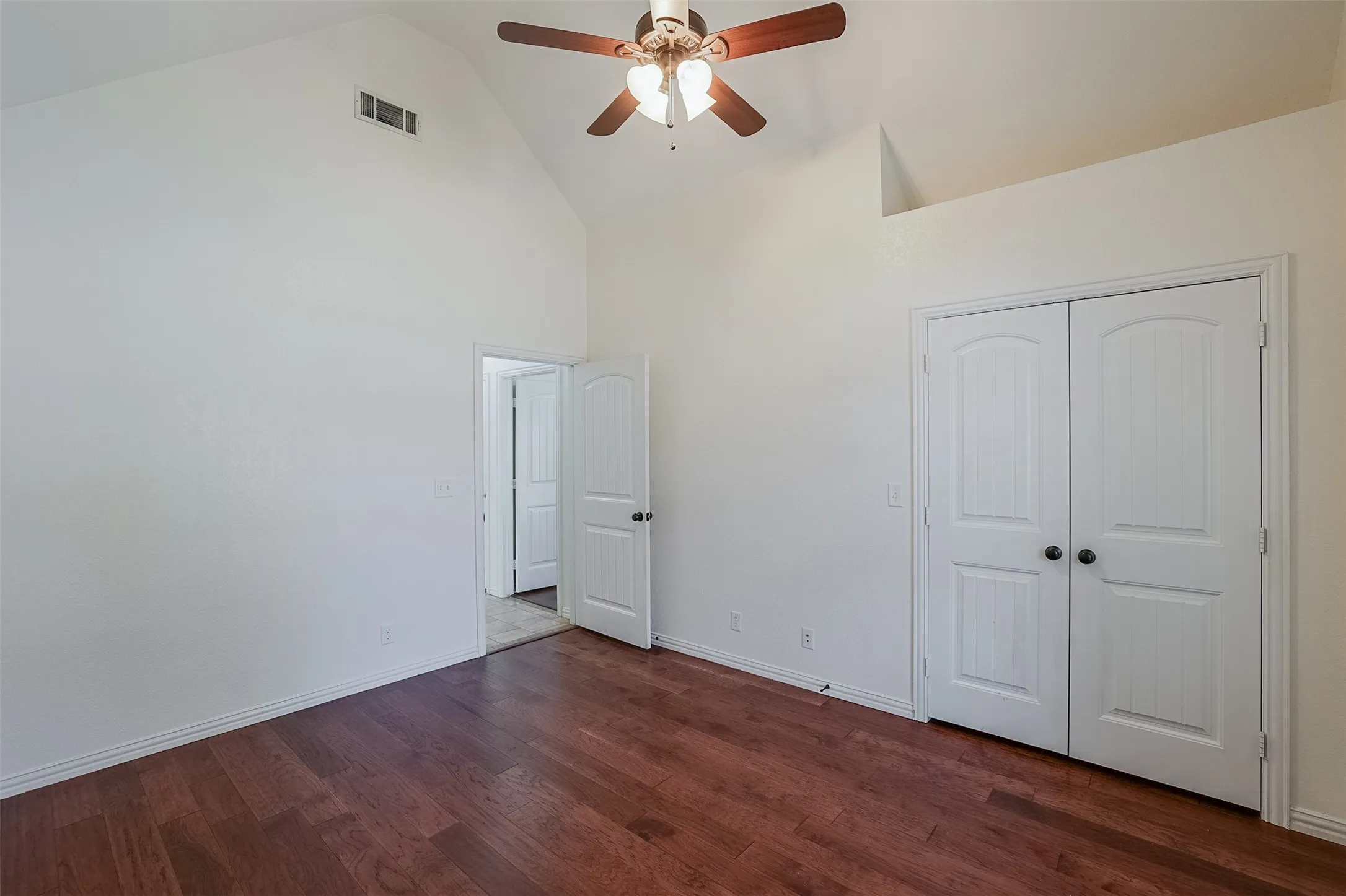 Vaulted ceiling, wood-finish flooring, ceiling fan with integrated lighting, dual white bi-fold doors, and white interior door