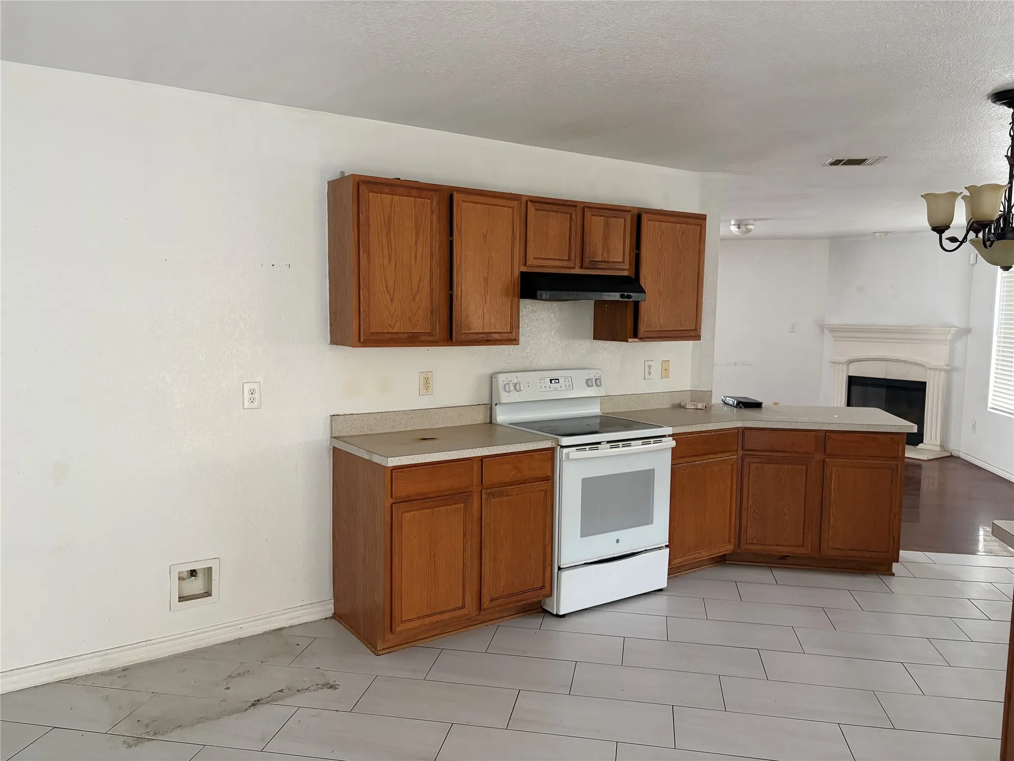Kitchen with wood cabinetry, light-toned countertops, white electric range, and a range hood
