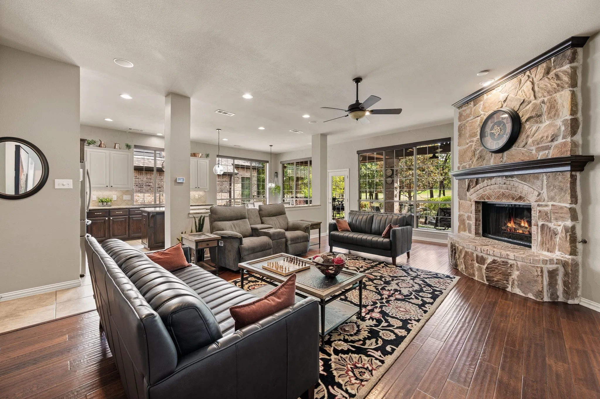 Inviting living room features rich wood floors, a dramatic stone fireplace & an open connection to the kitchen. It also features in-ceiling speakers.