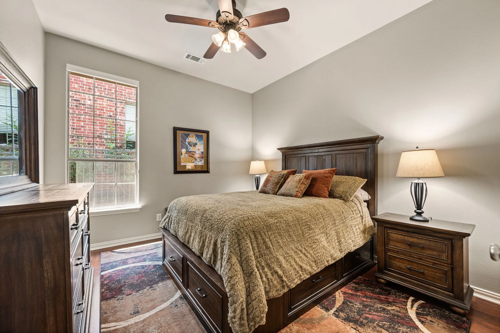 Comfortable secondary bedroom features wood flooring, a ceiling fan & a large window for natural light.