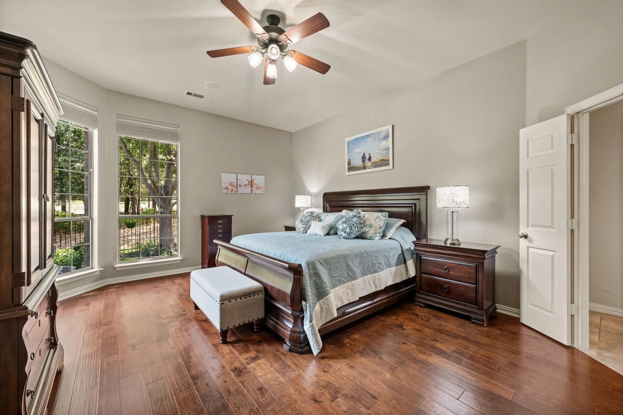 Spacious primary suite features wood floors, a ceiling fan & peaceful views through tall windows.  It also has in-ceiling speakers!
