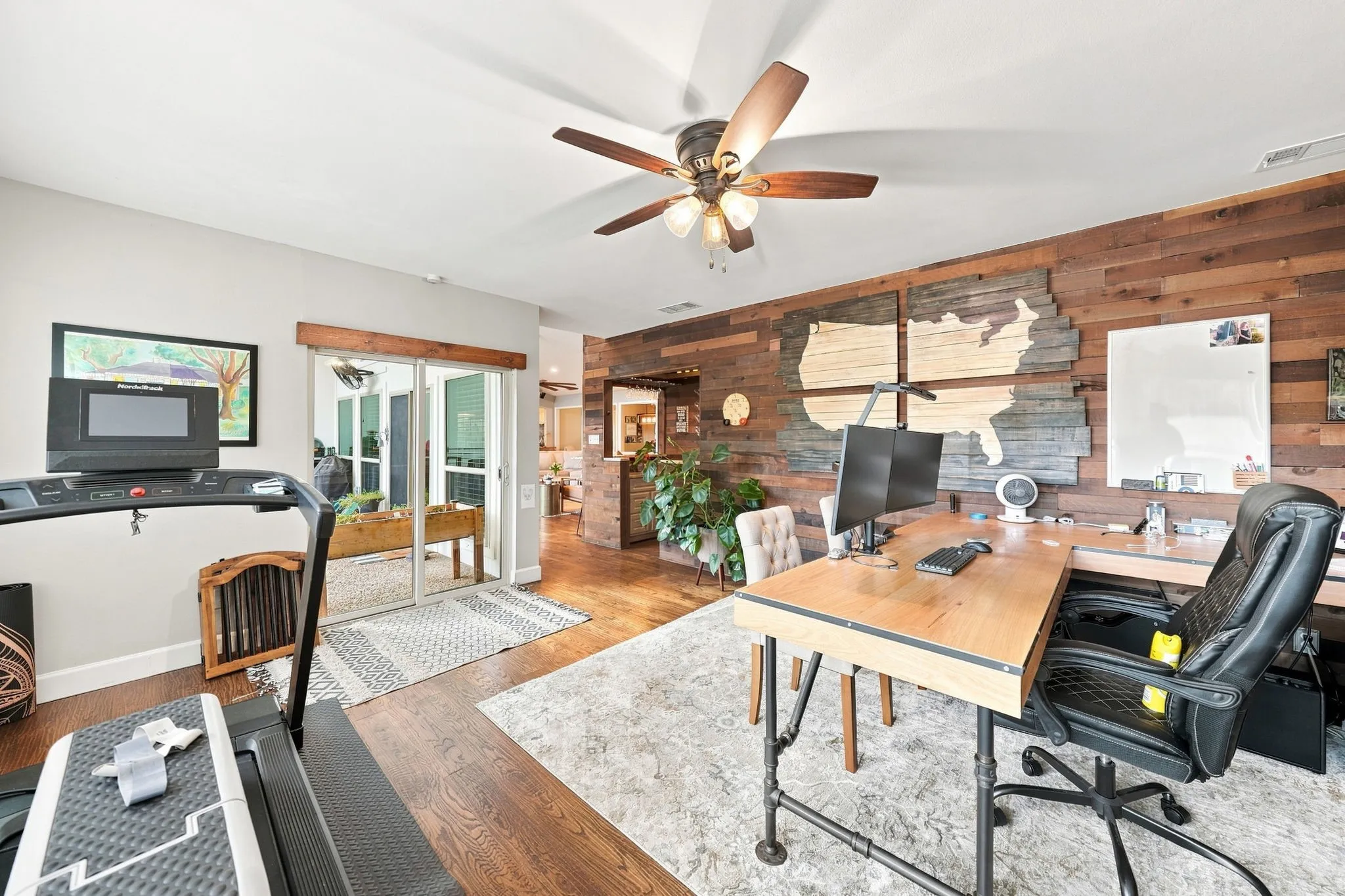 Wood-finish flooring throughout, featuring a wood accent wall, a ceiling fan with integrated lighting, and sliding glass doors