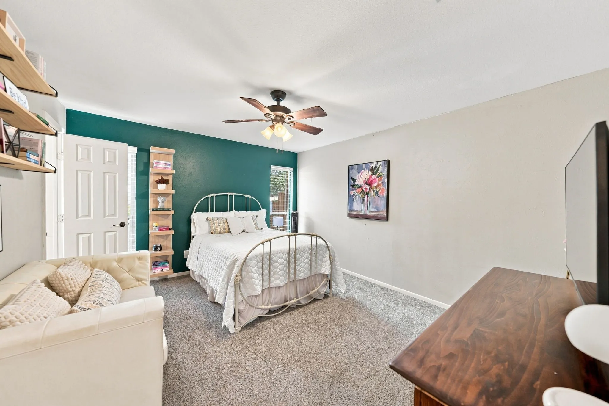 Carpeted bedroom featuring a textured accent wall, ceiling fan with integrated lighting, window with blinds, and white paneled door