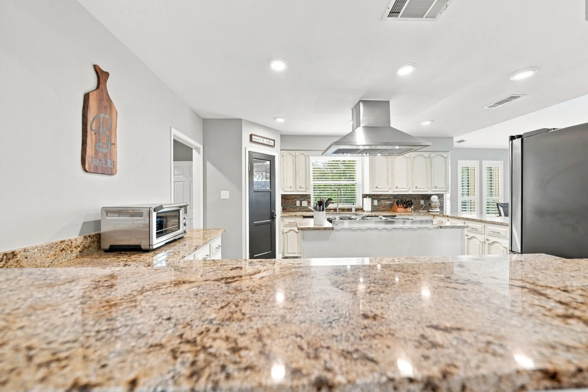 Kitchen featuring granite countertops, white cabinetry, a stainless steel range hood, recessed lighting, and a kitchen island