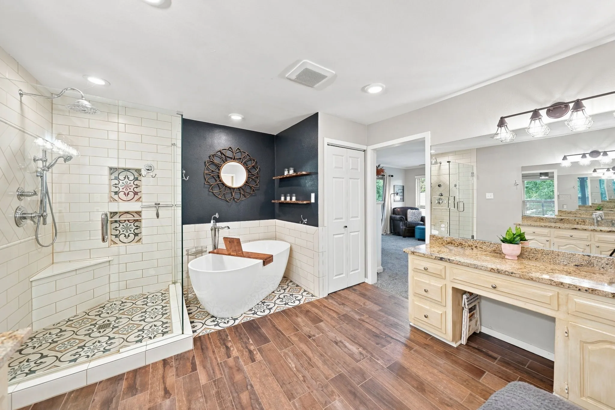Freestanding soaking tub with decorative floor tiling, walk-in shower with tiled walls and built-in bench, dual vanity with granite countertop, wood-finish flooring, and recessed lighting