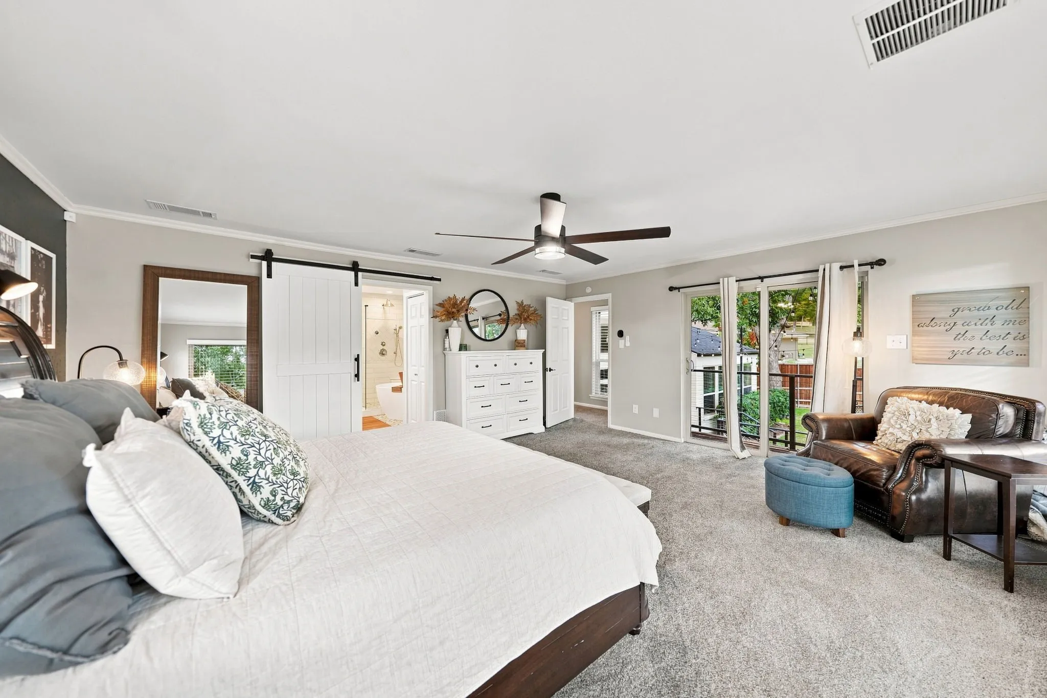 Spacious room featuring light gray wall paint, a ceiling fan, sliding glass doors, a white barn door, and gray carpeting
