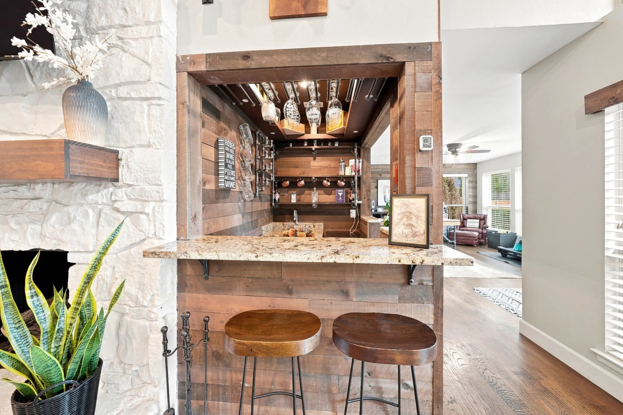 Sophisticated wet bar featuring brick surround with open shelving, mirrored back panel, pendant lighting, and two wood-seat bar stools