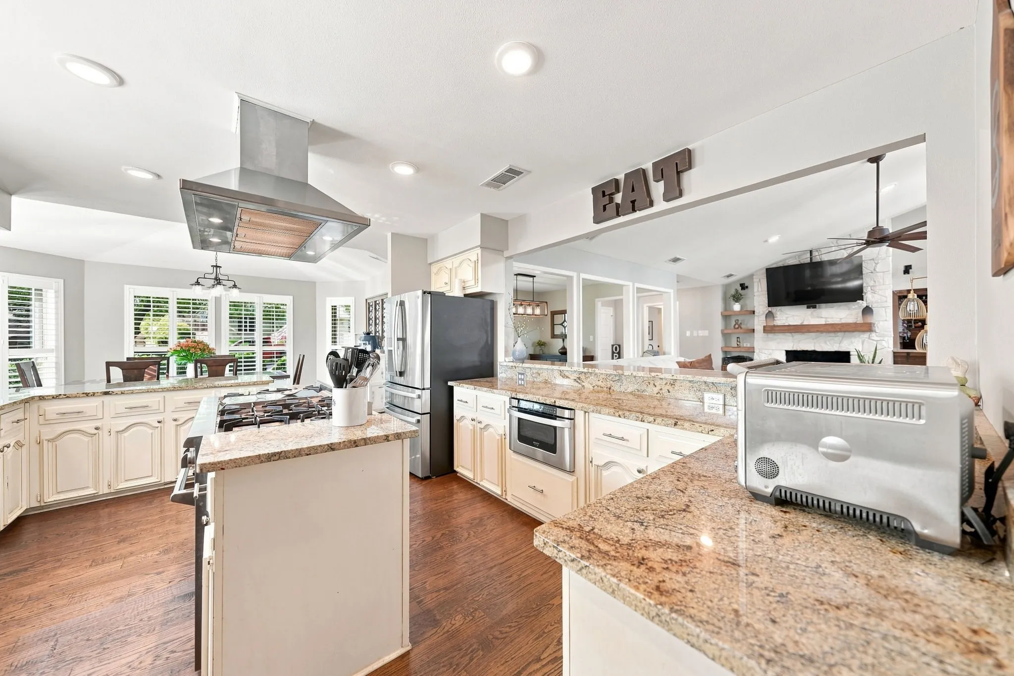 Kitchen featuring wood-finish flooring, stone countertops, white cabinetry, a stainless steel range hood, and recessed lighting