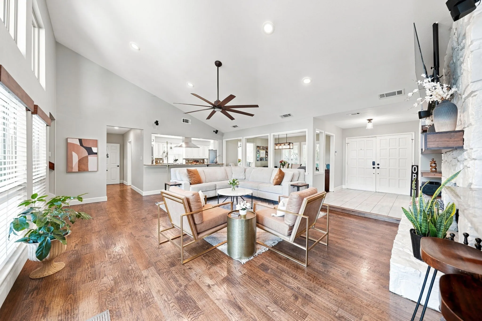Vaulted ceiling with a ceiling fan, recessed lighting, wood-finish flooring, stone-clad fireplace, and double-door entry