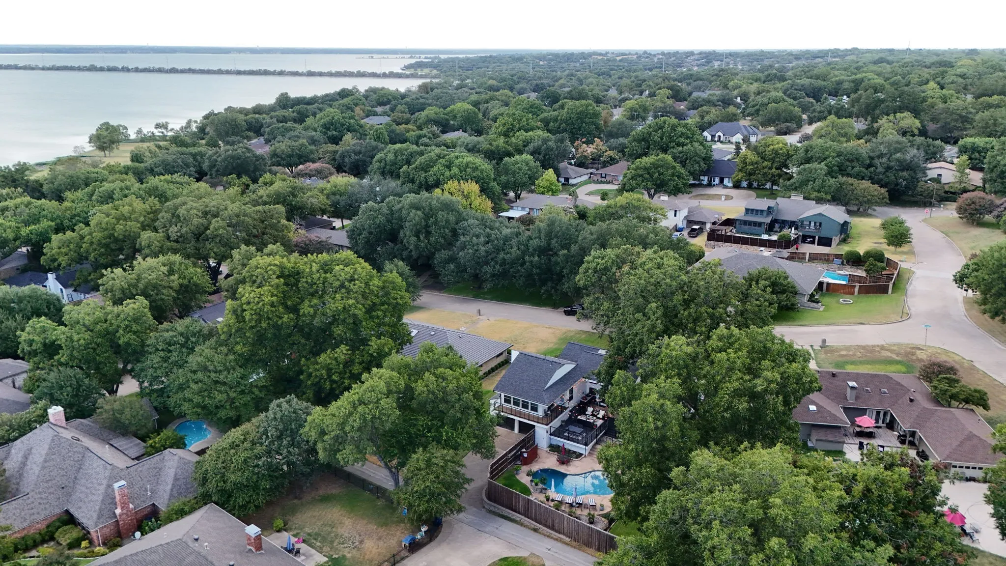 Aerial perspective showcasing properties, extensive tree canopy, and a body of water