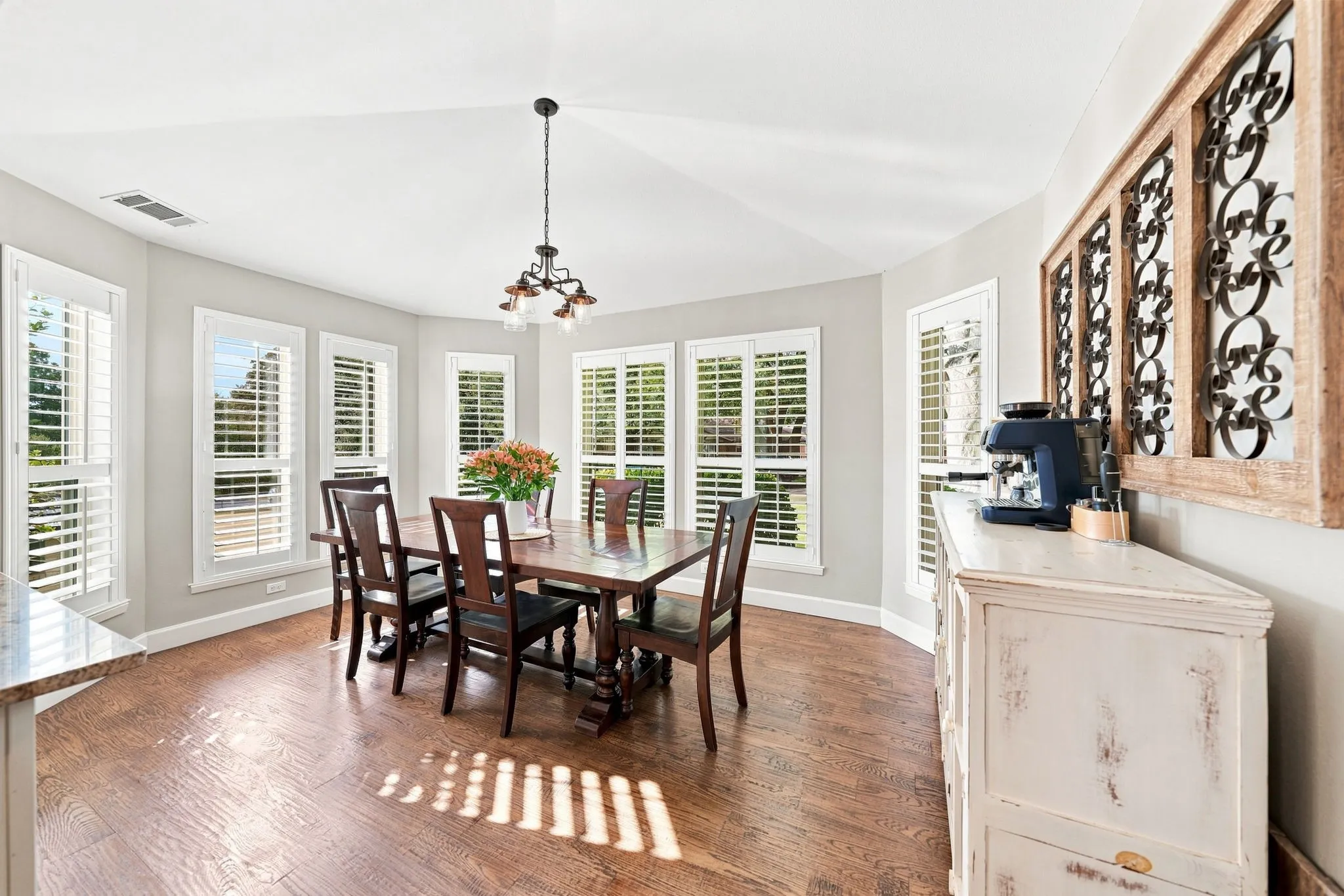 Vaulted ceiling with an architectural chandelier, multiple windows with white plantation shutters, rich wood-finish flooring, and light gray wall paint