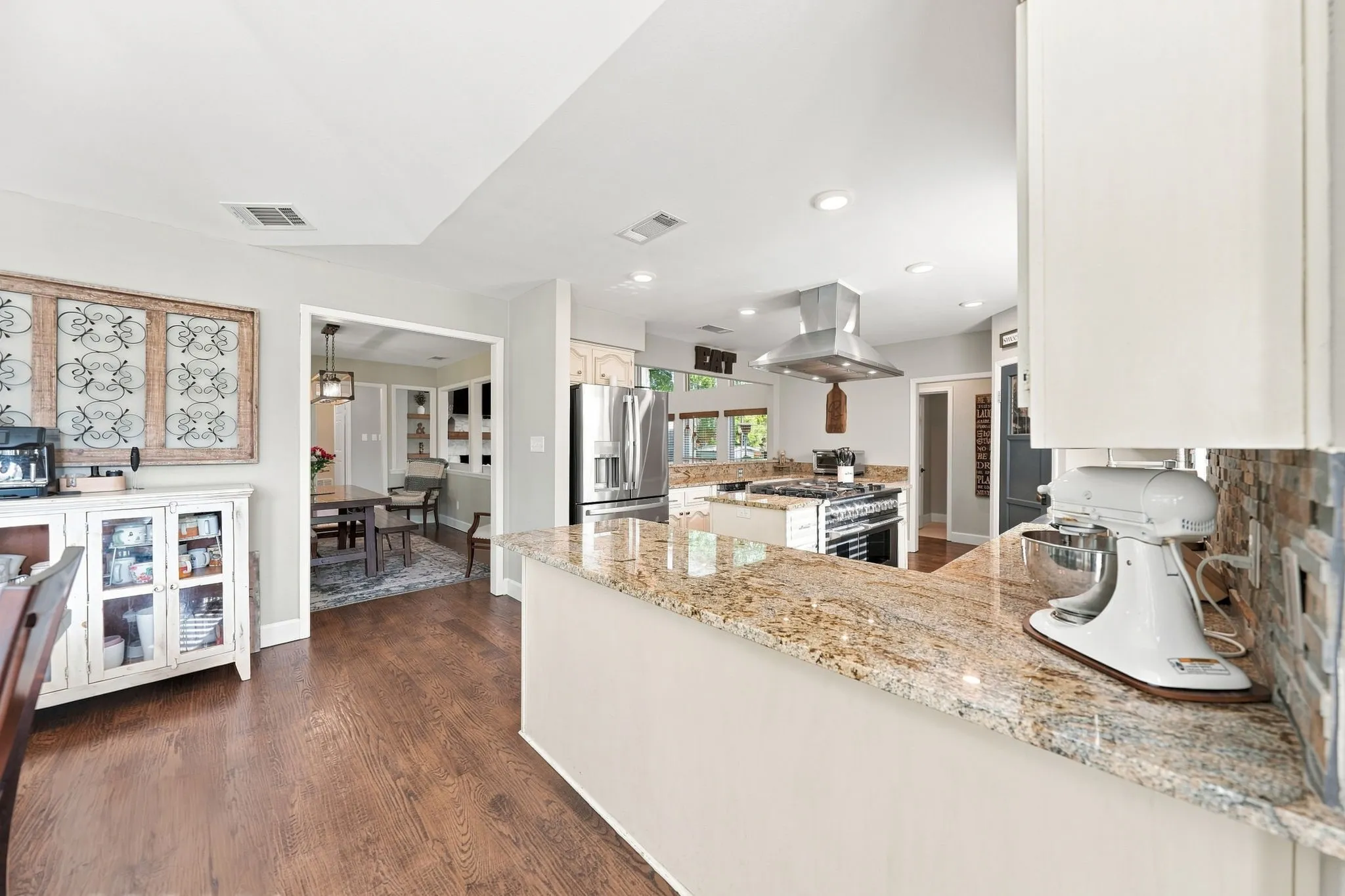 Kitchen featuring a granite countertop, tile backsplash, stainless steel range hood, and wood-finish flooring
