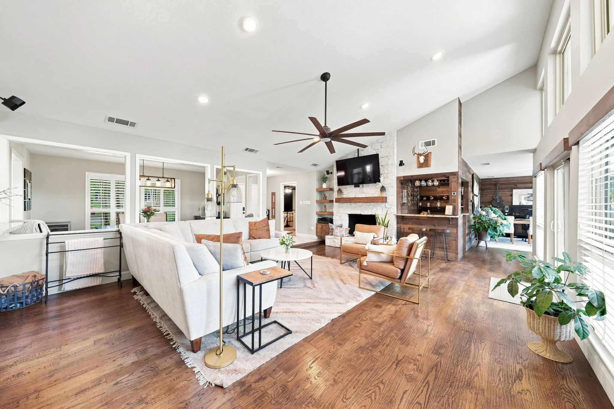 Vaulted ceiling with wood-finish fan, wood-finish flooring, stone-clad fireplace, built-in wet bar, and transom windows