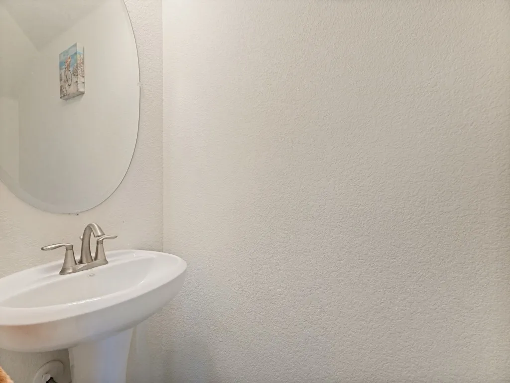 Pedestal sink with a brushed nickel faucet and an oval mirror