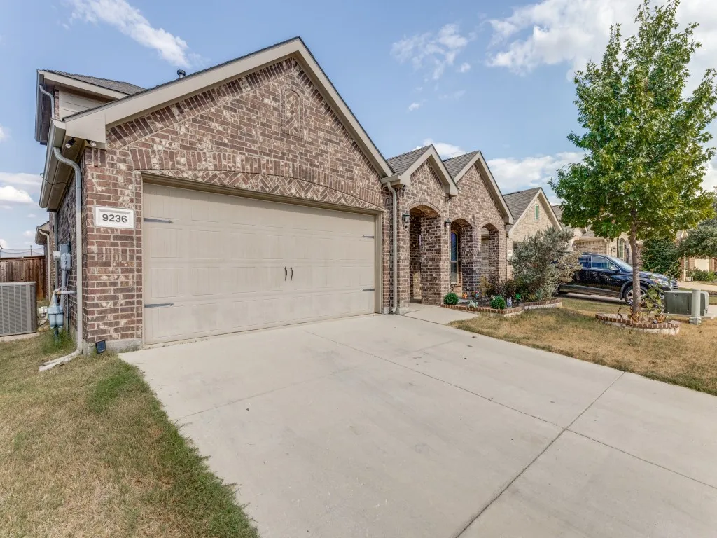 Brick facade with arched entryway, concrete driveway, and attached garage