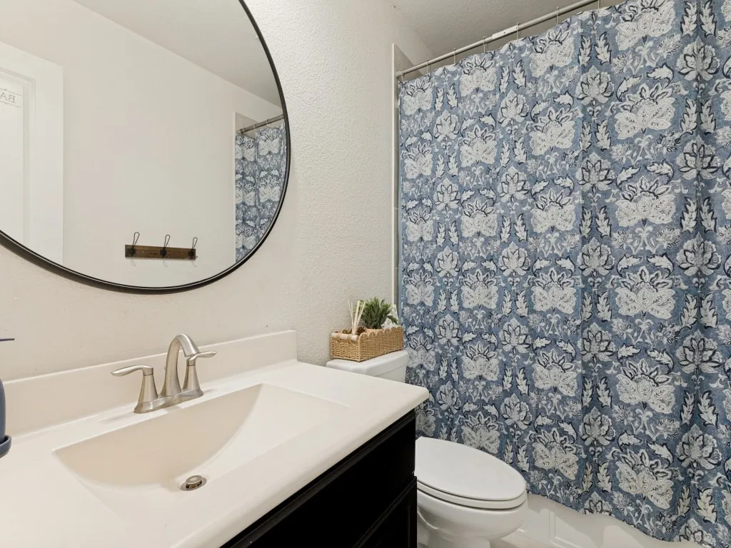 White countertop with an integrated sink, brushed nickel faucet, and a round mirror