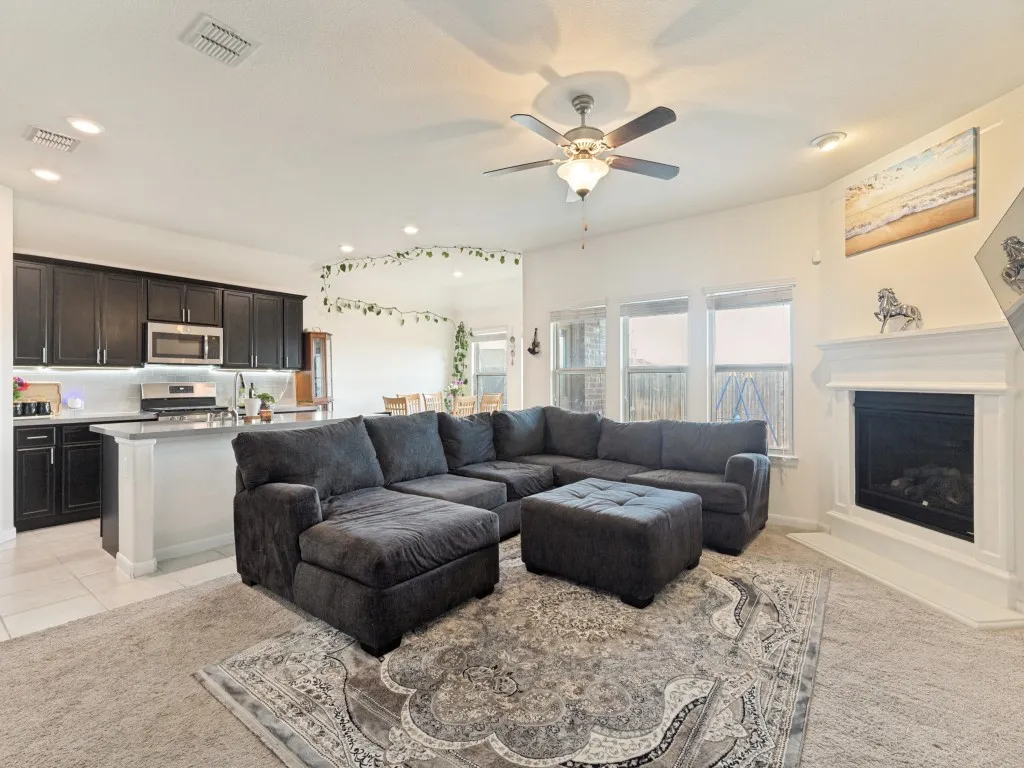 Open-concept living space featuring a kitchen with dark cabinetry and stainless steel appliances, a living area with a fireplace, and a ceiling fan