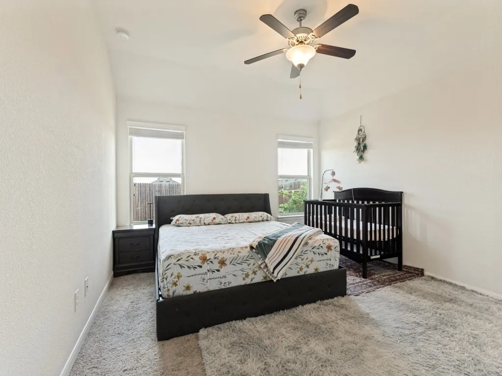Vaulted ceiling with a ceiling fan, two windows with blinds, and light-colored wall-to-wall carpeting