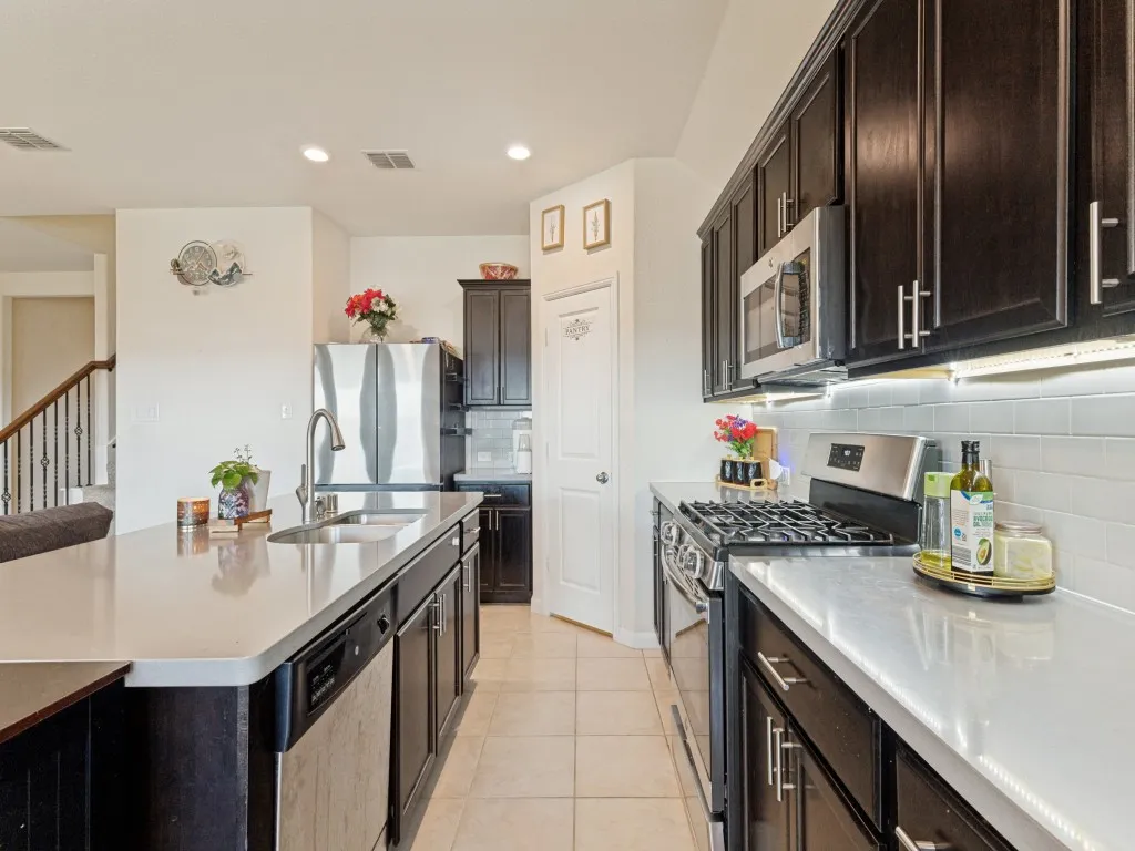Kitchen featuring dark wood cabinetry, light-toned countertops, stainless steel appliances, and a white subway tile backsplash