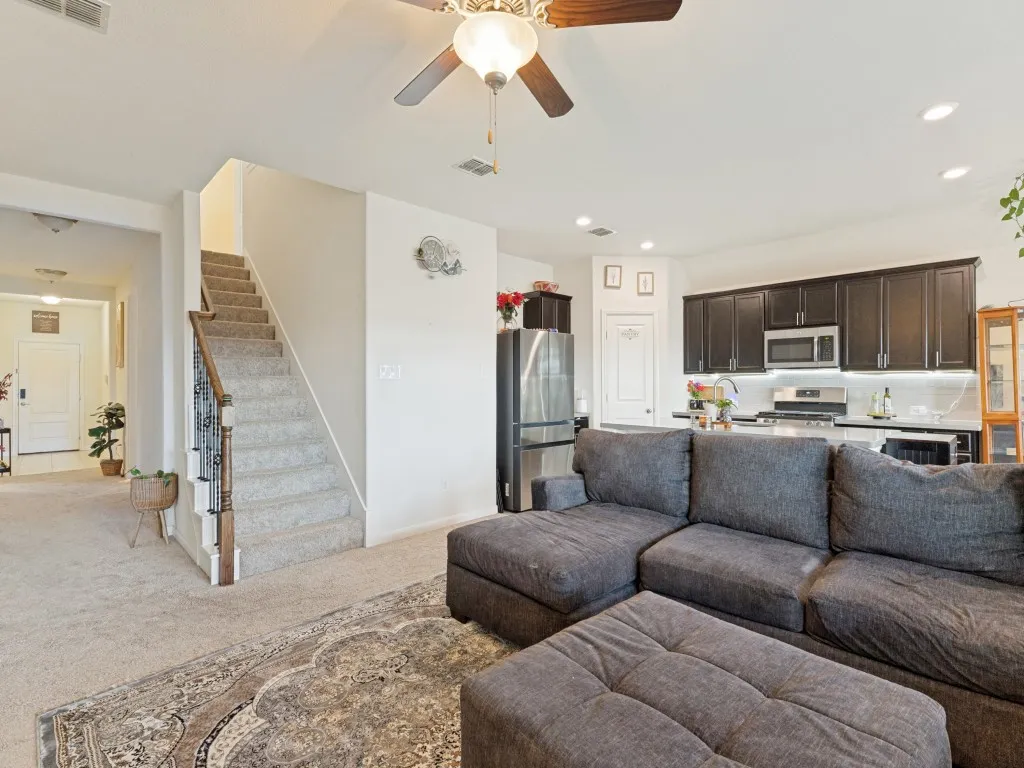 Open-concept living area with ceiling fan, recessed lighting, carpeted flooring, and staircase with wrought iron balusters
