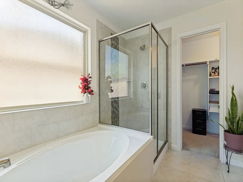 Soaking tub with tile surround, glass-enclosed shower, and a privacy window