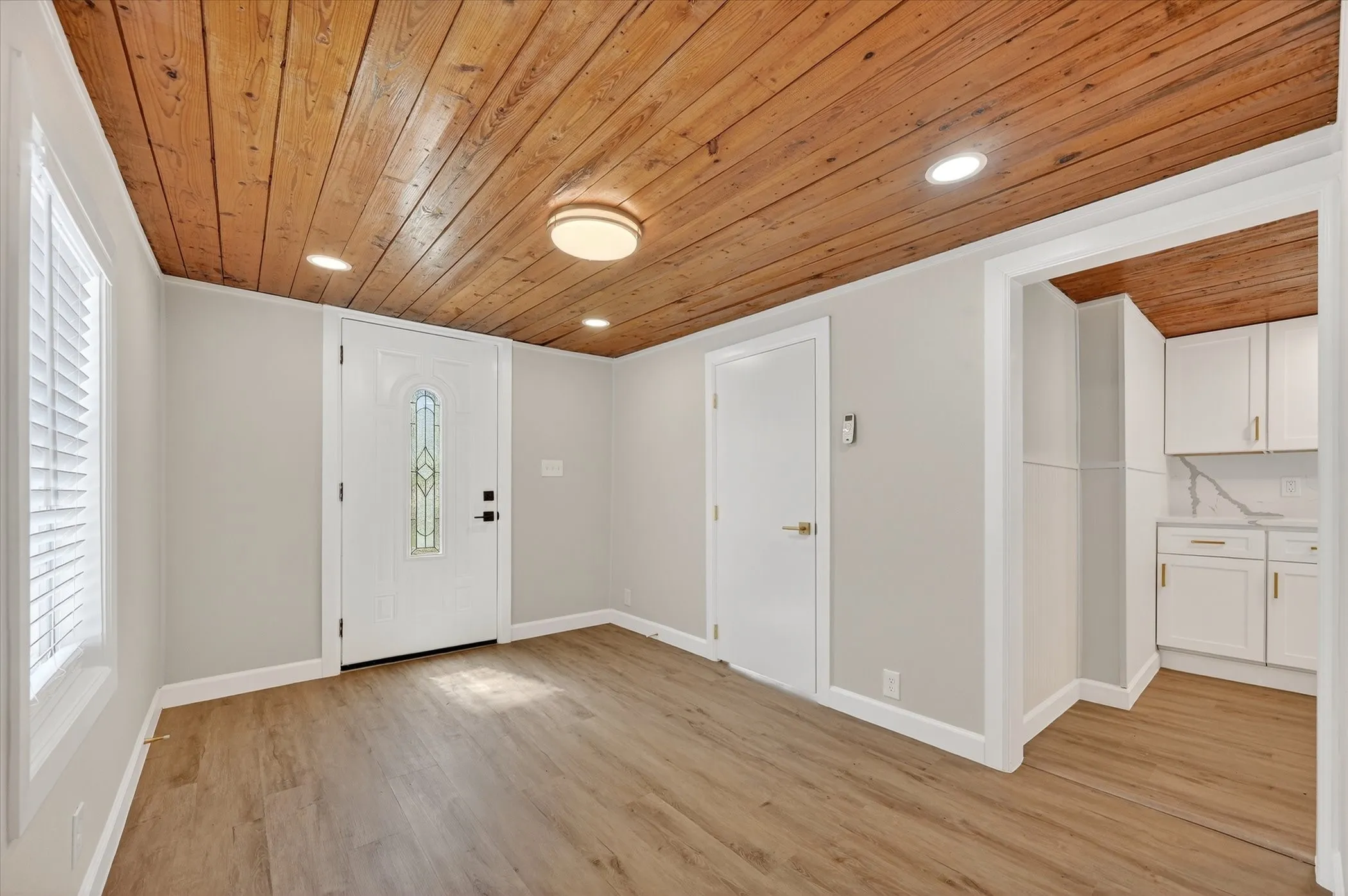 Wood plank ceiling with recessed lighting, wood-finish flooring, white entry door with decorative glass, and white window shutters