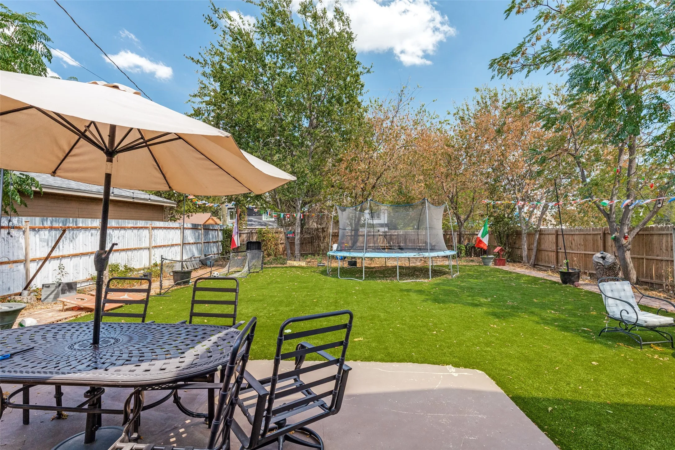 Expansive backyard featuring a concrete patio, artificial turf, and mature perimeter trees