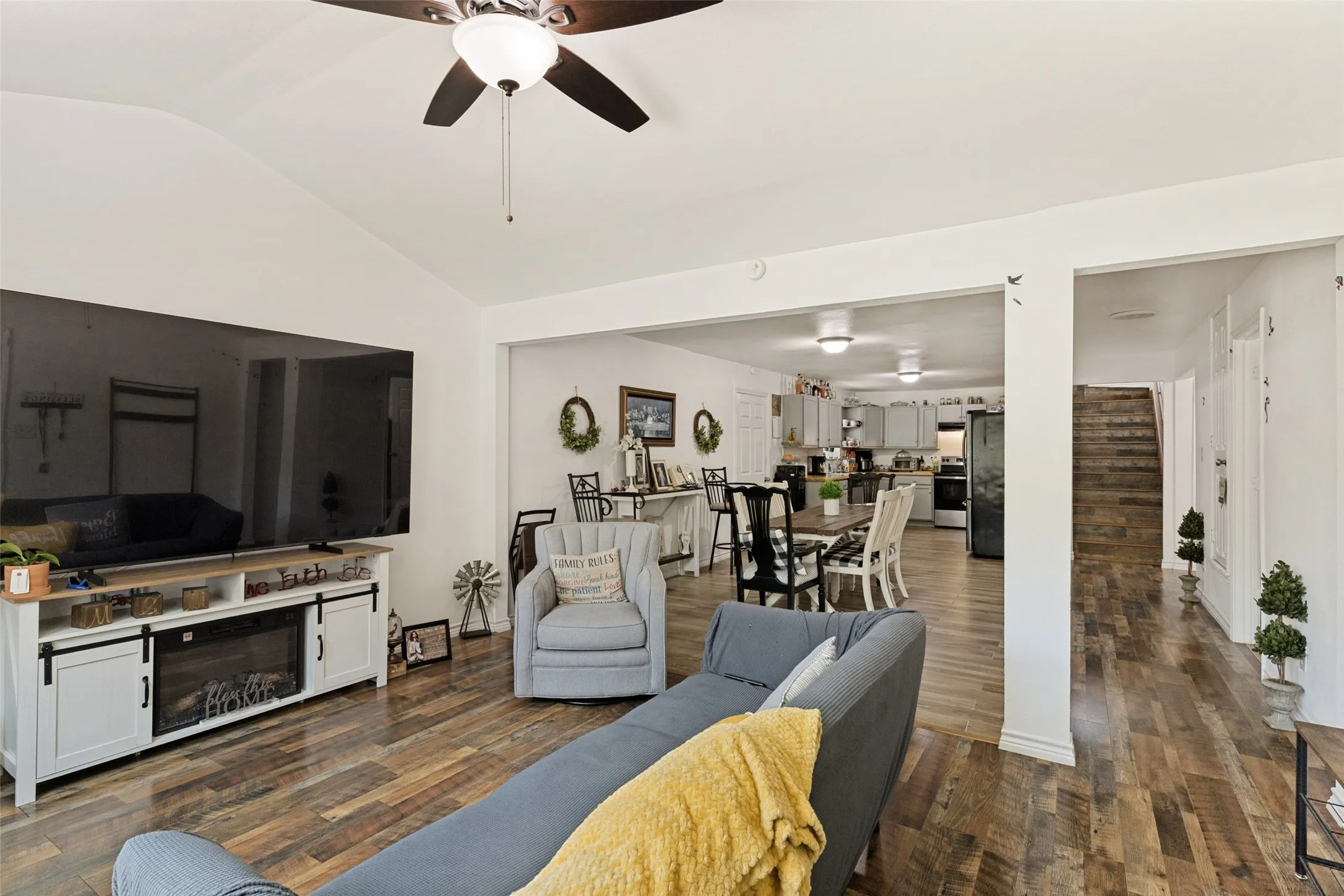Vaulted ceiling with a ceiling fan, wood-finish flooring, and an entertainment console with an electric fireplace