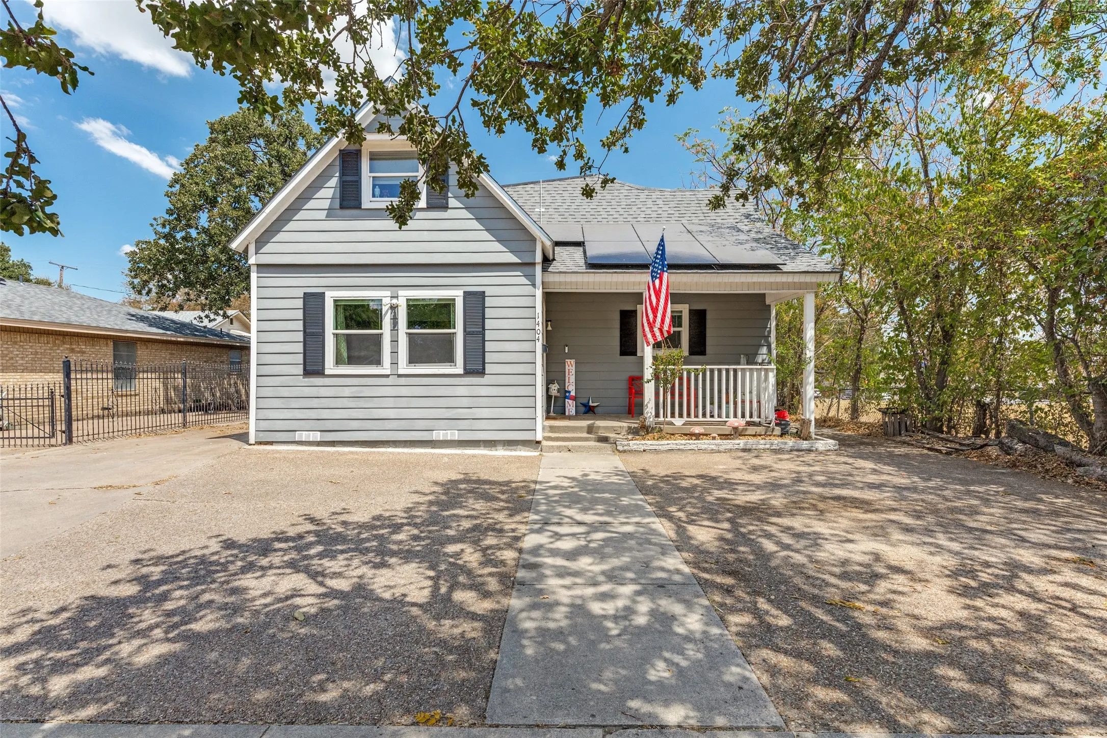 Single-family residence featuring a covered front porch with white railing, gray horizontal siding, and dark shutters