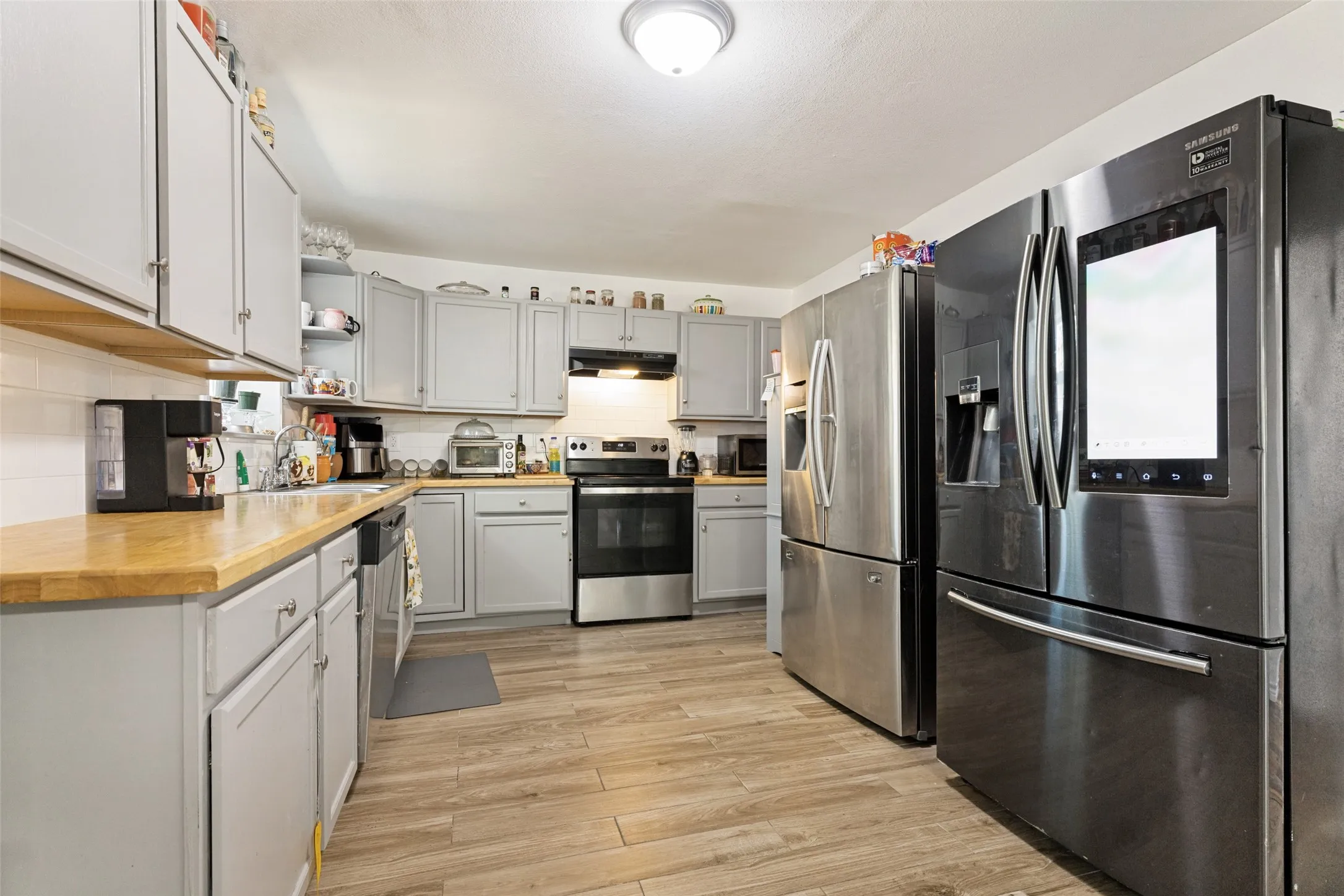 Kitchen featuring wood-finish flooring, light grey cabinetry, light wood-finish countertops, stainless steel appliances, and a white subway tile backsplash