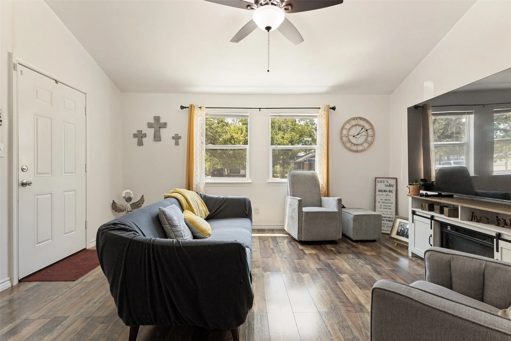 Vaulted ceiling with a ceiling fan, wood-finish flooring, white paneled door, and dual windows providing natural light