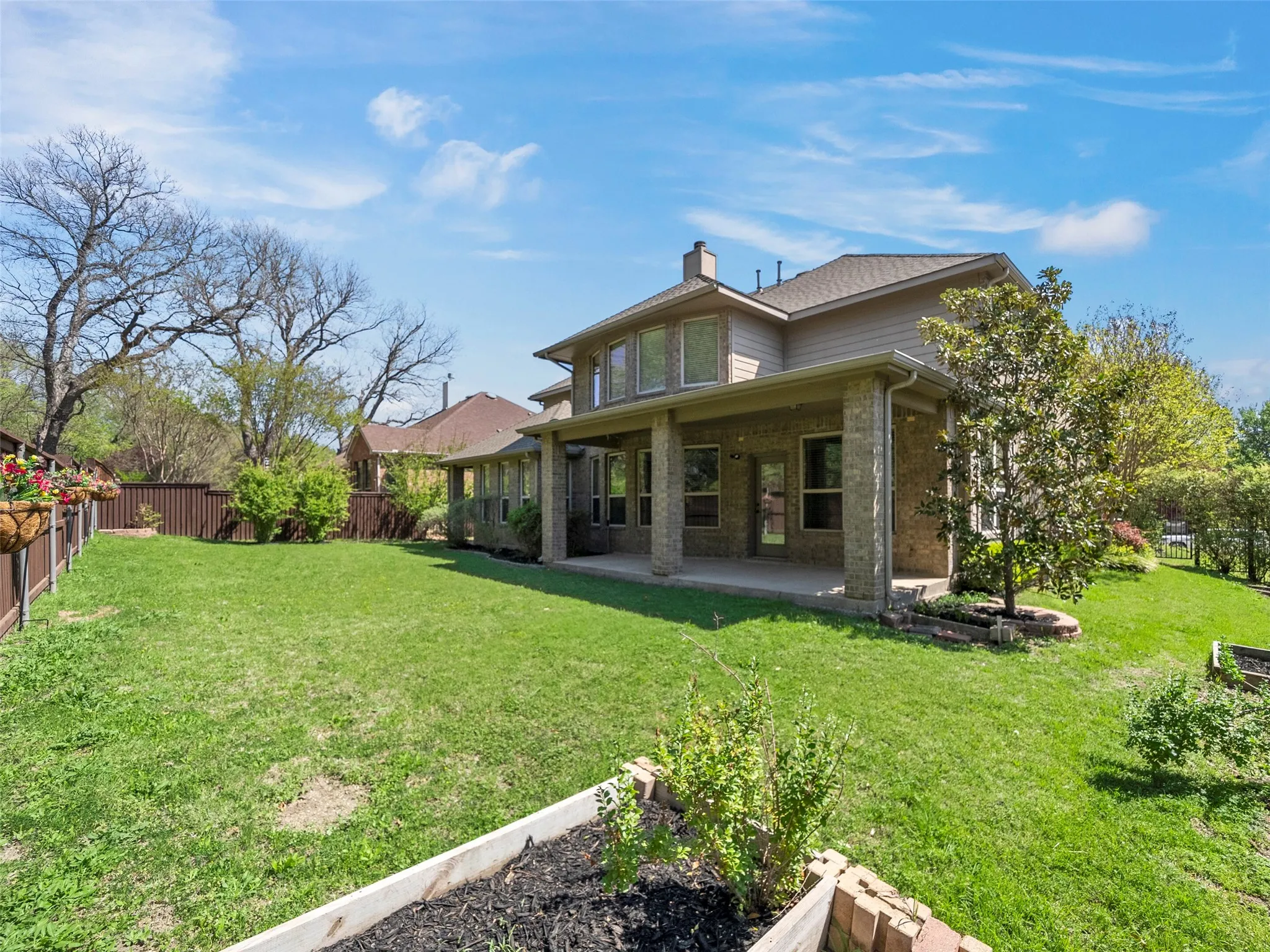 Expansive backyard featuring a manicured lawn, a covered patio with stone columns, and raised garden beds