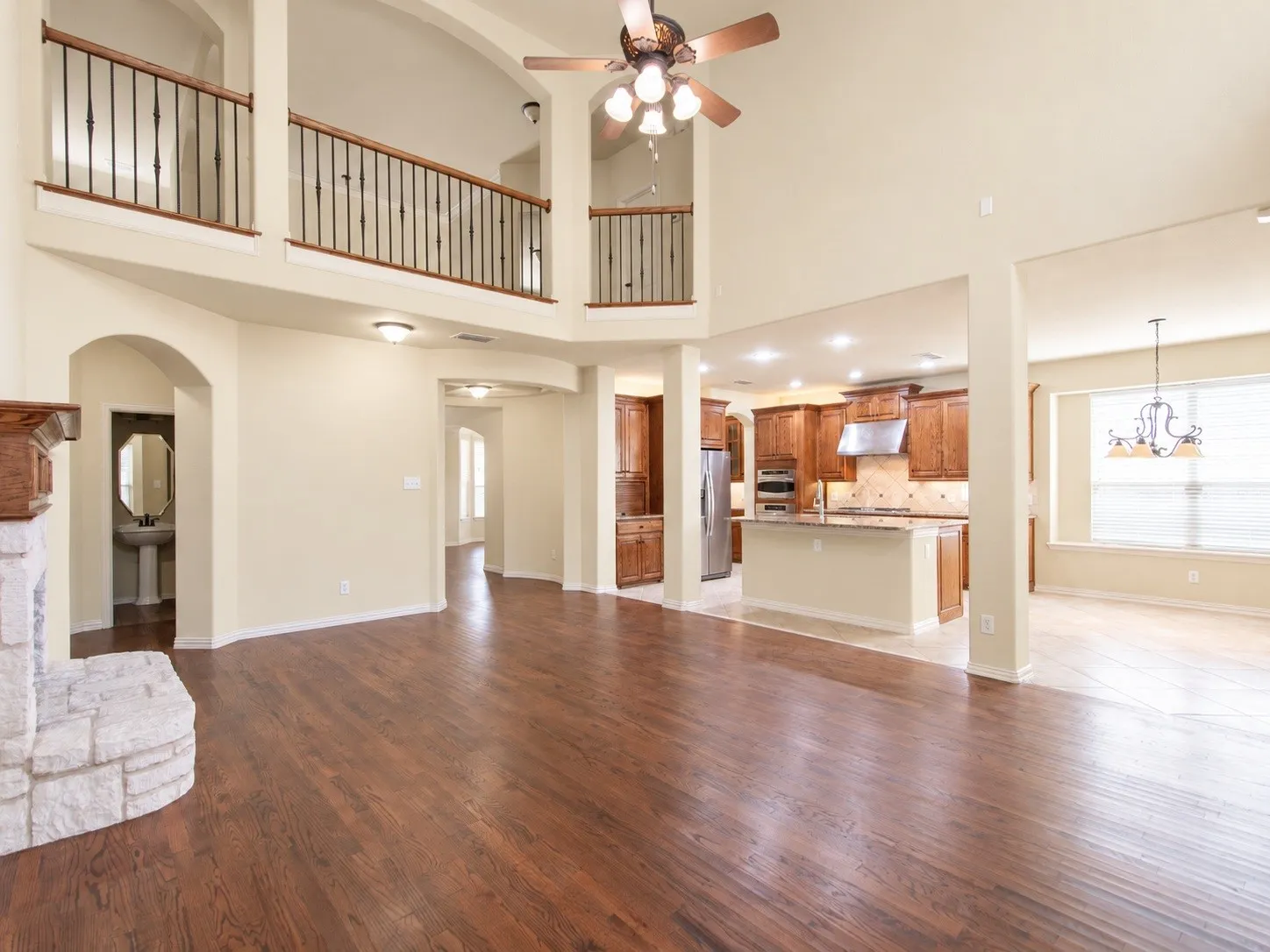 Expansive living area with wood-finish flooring, a stone fireplace, and an open-concept kitchen featuring wood cabinetry and an island