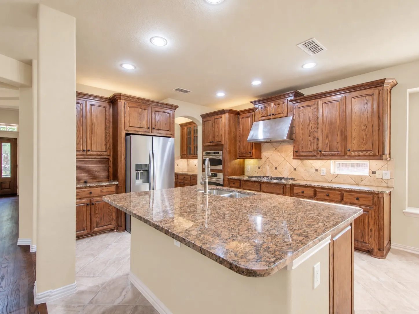 Kitchen featuring wood cabinetry, an island with stone countertop, stainless steel appliances, recessed lighting, and tile flooring
