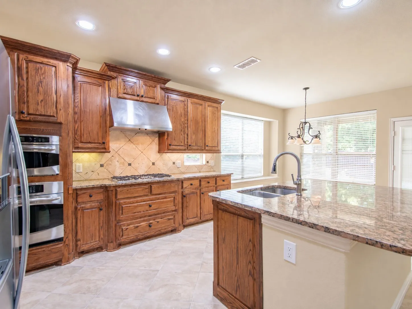 Kitchen featuring wood cabinetry, stainless steel appliances, a tile backsplash, granite countertops, and recessed lighting