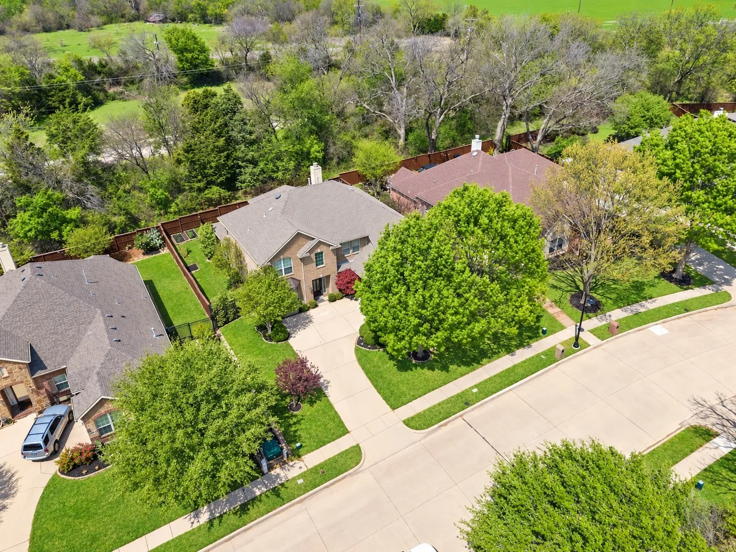 Two-story brick exterior, attached garage, concrete driveway, and a fenced backyard with manicured lawn