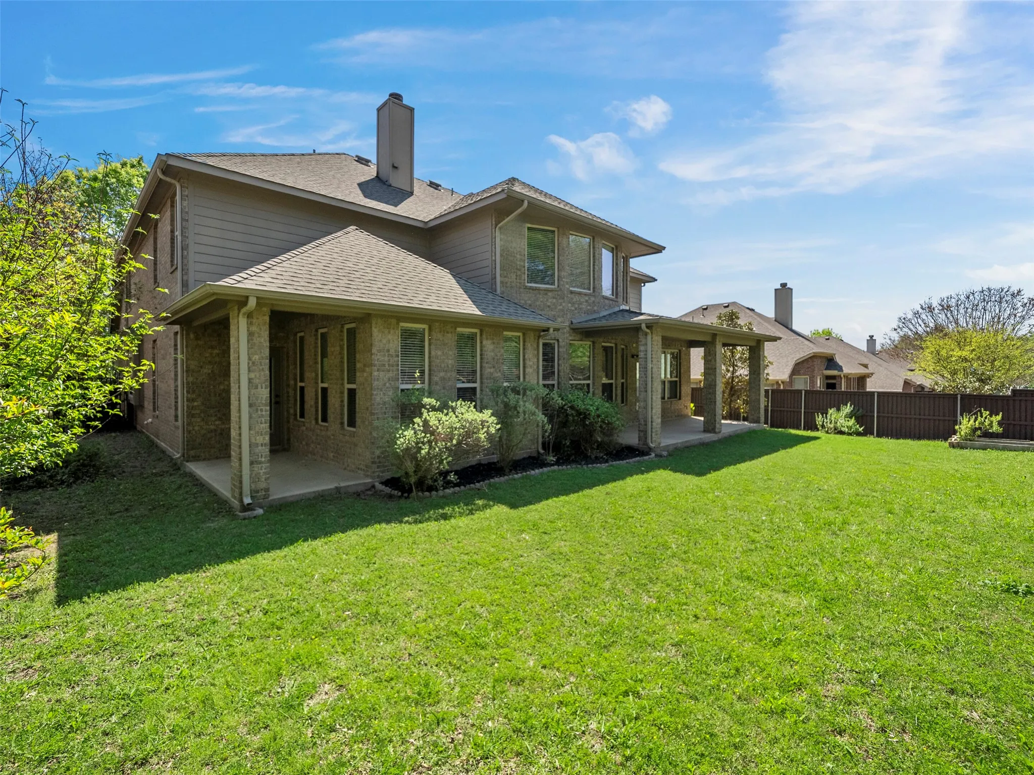 Expansive grass lawn with a covered patio, brick and siding exterior, and a privacy fence