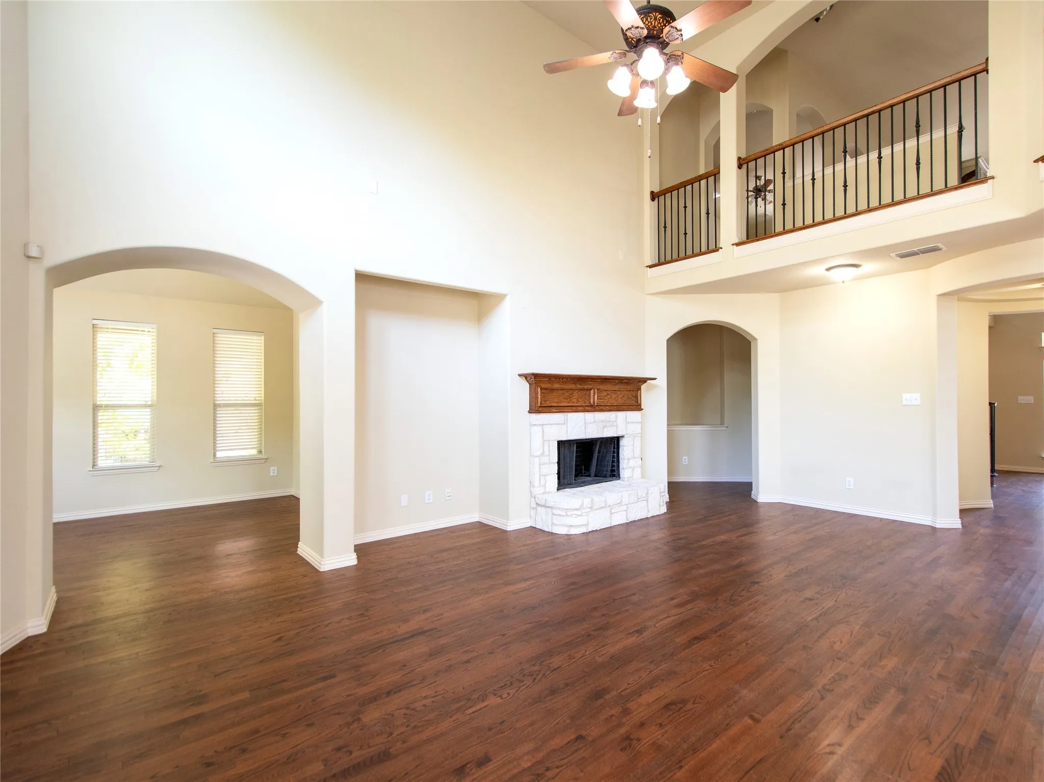 Two-story living area featuring wood-finish flooring, a stone-surround fireplace with a wood mantle, and arched doorways