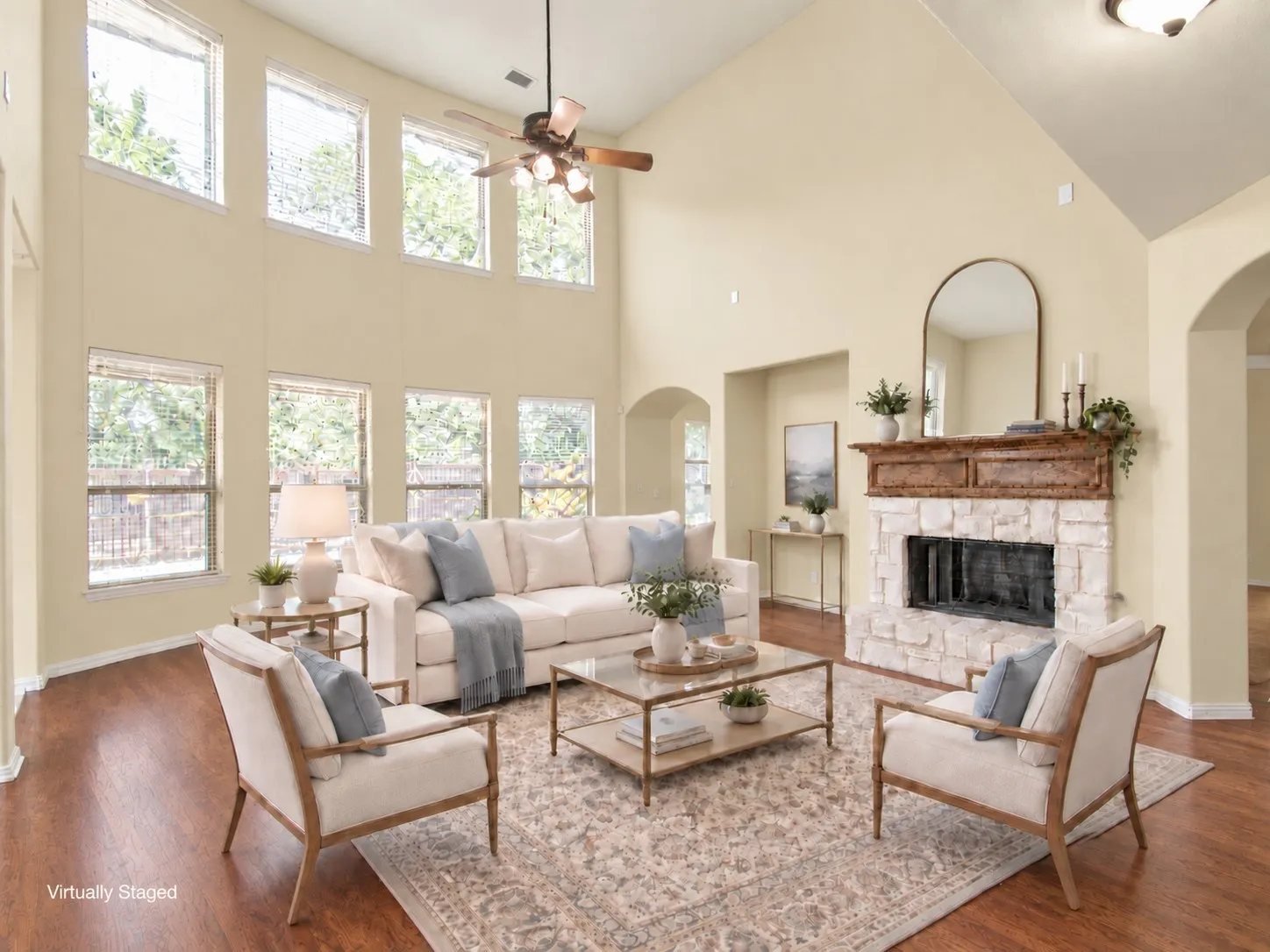 Vaulted ceiling with a ceiling fan, stone fireplace with a wood mantel, multiple windows, archway, and wood-finish flooring