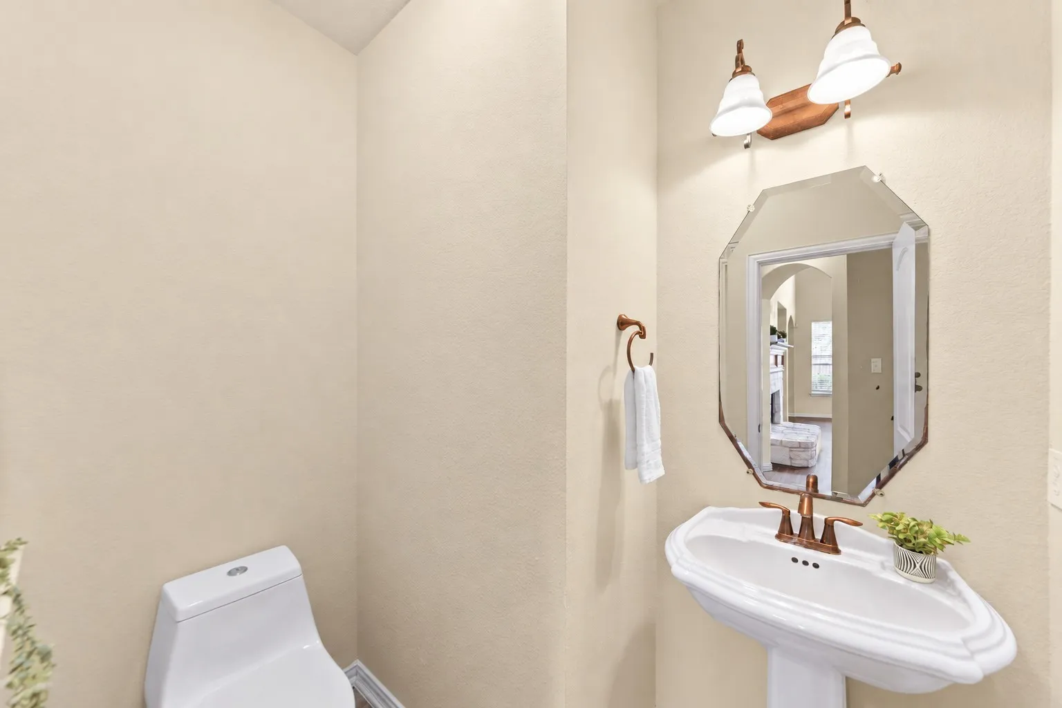 Pedestal sink with a bronze-finish faucet, octagonal beveled mirror, and a two-light wall sconce