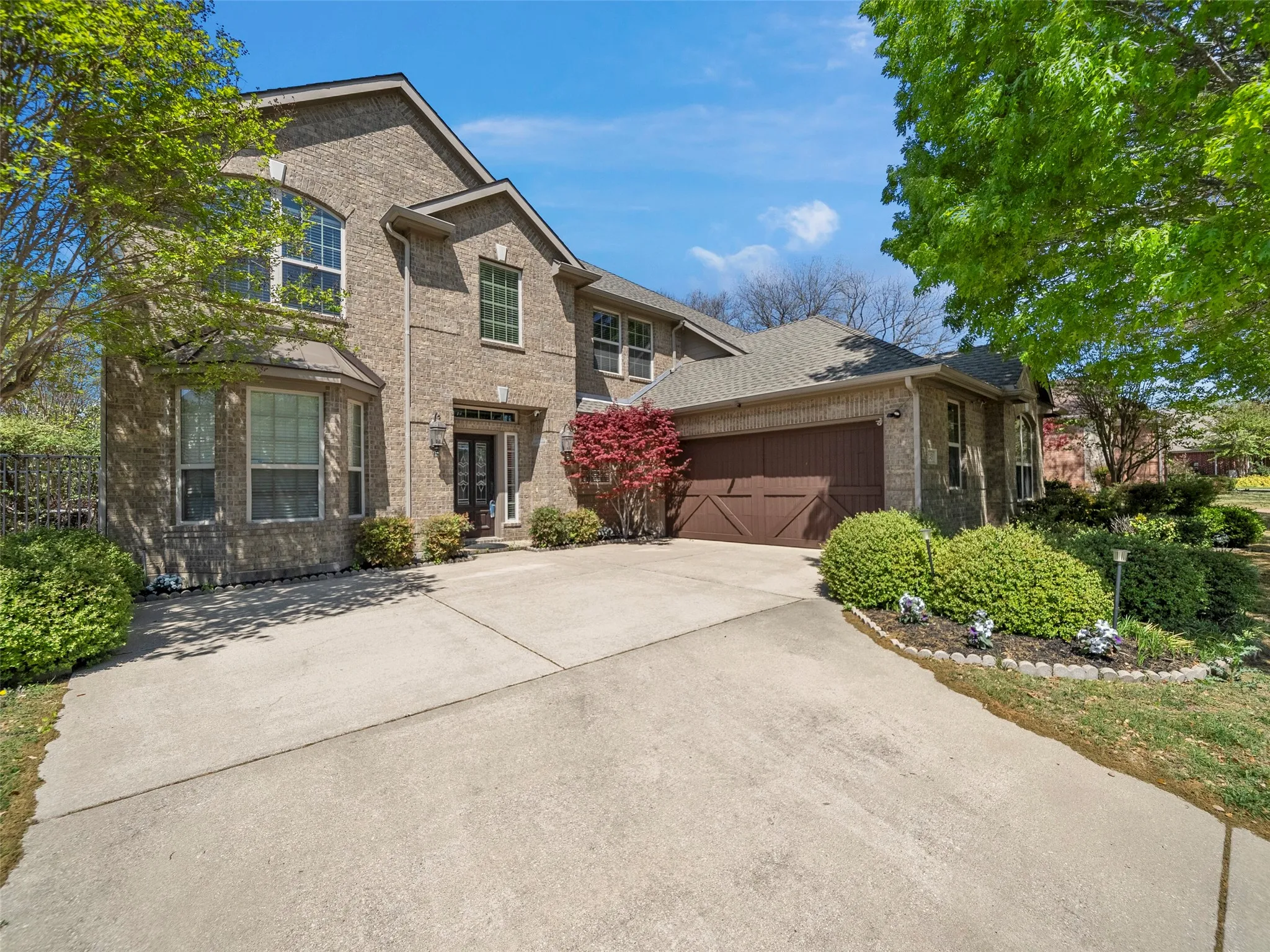 Brick exterior featuring a two-car garage with wood-finish doors, an arched window, and a concrete driveway