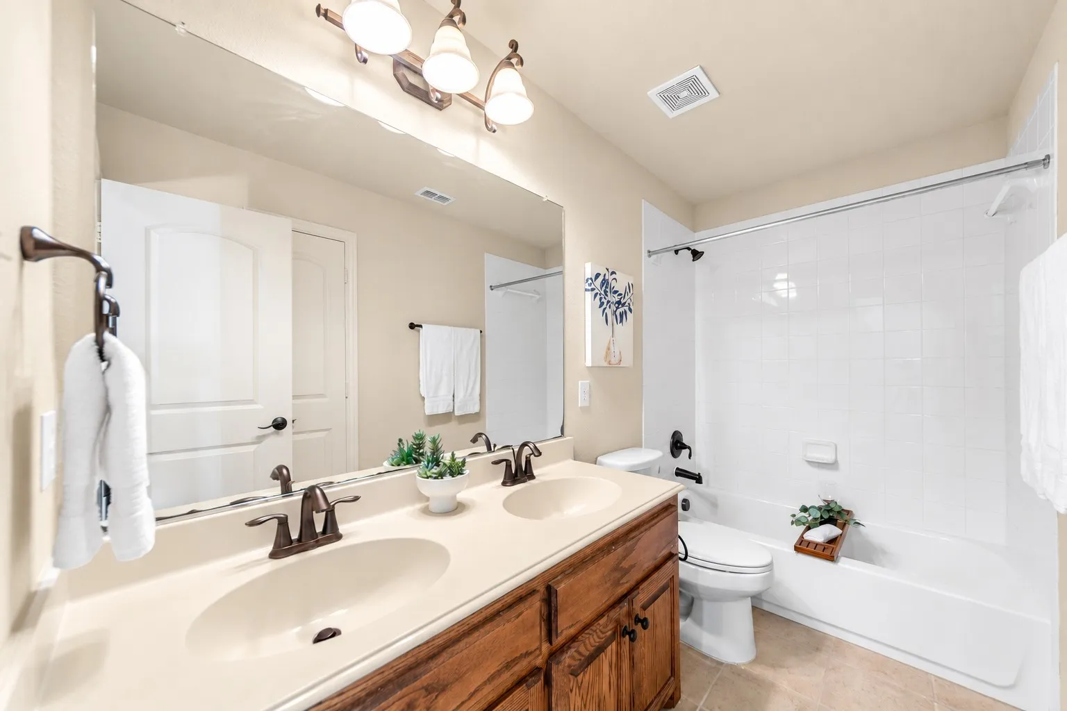 Dual vanity with integrated sinks, bronze-finish fixtures, a full-width mirror, and a combination shower-tub with a tiled surround