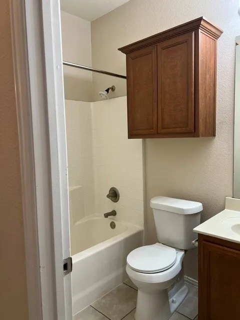 White tub and shower combination with tiled surround, wall-mounted wood-finish cabinet, and tiled flooring