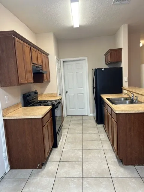 Galley kitchen featuring wood-finish cabinetry, light-toned countertops, and tile flooring
