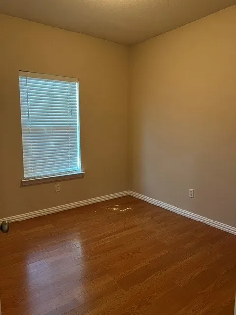 Wood-finish flooring with white trim, a single window with blinds, and neutral wall tones