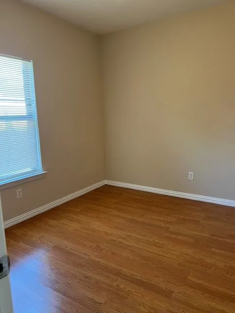 Wood-finish flooring with white trim, neutral wall color, and a window with blinds
